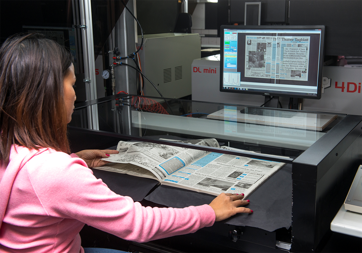 Die Mitarbeiterin einer Scanfirma scannt einen Band des «Thuner Tagblatts». Dabei blättert sie die Seiten von Hand um, fährt die Glasplatte auf das Papier, damit sie Seiten flach liegen, und fotogafiert immer eine Doppelseite.